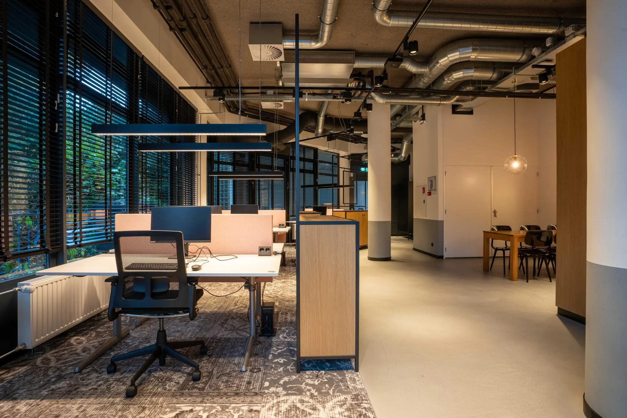 Modern ingericht kantoor aan de 1e Hogeweg met werkplekken, vergadertafel en zichtbare ventilatiebuizen.